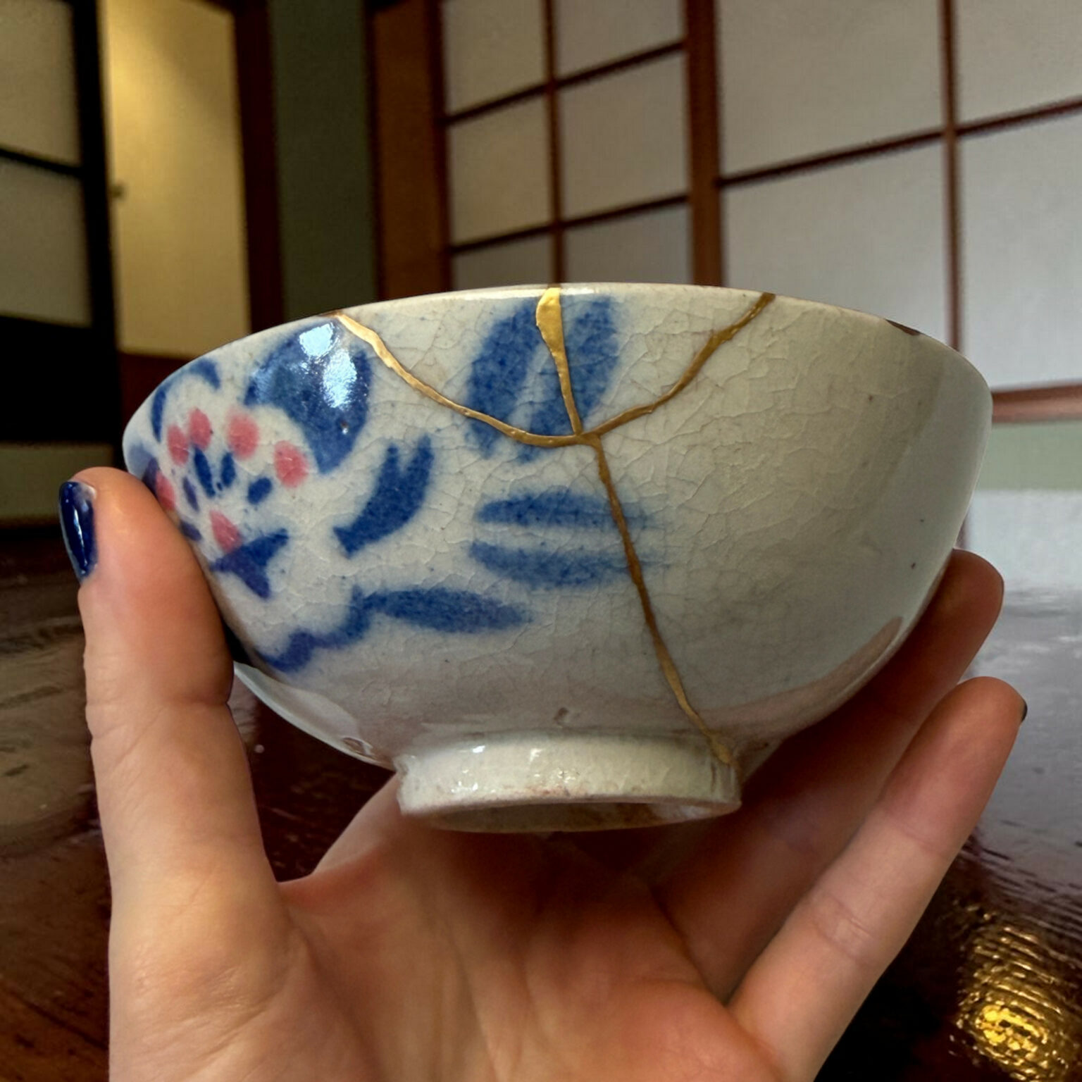 Close-up of a blue‑and‑white ceramic bowl with gold decorative lines, held by hands.