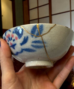 Close-up of a blue‑and‑white ceramic bowl with gold decorative lines, held by hands.