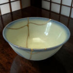 Close-up of a pale blue ceramic bowl on a dark wooden table, with thin tan string laid across its surface.