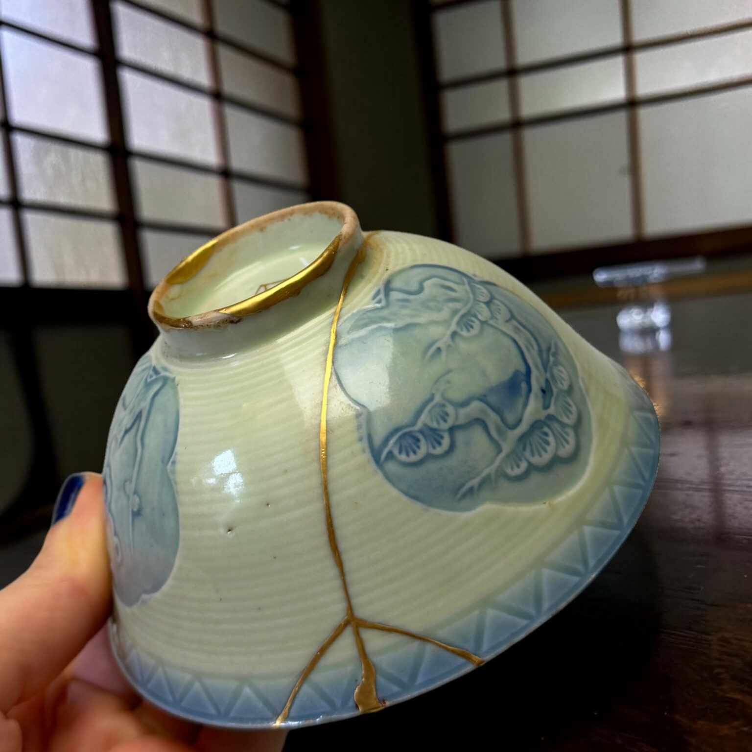 Close-up of a pale blue ceramic vase with floral patterns, held by a hand with a yellow string wrapped around its neck.