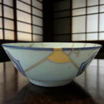 Blue ceramic bowl with a gold string tied around it sits on a dark wooden surface, close-up view.