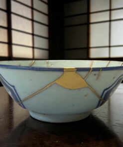 Blue ceramic bowl with a gold string tied around it sits on a dark wooden surface, close-up view.