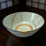 Close-up of a light blue ceramic plate with a blue rim and gold decorative lines on a dark wooden table.