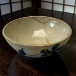 Ceramic bowl repaired with gold kintsugi seams on a dark wooden table.