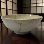 Ceramic bowl with a braided cord looped around its rim on a dark wooden table; a geometric grid backdrop in the background.