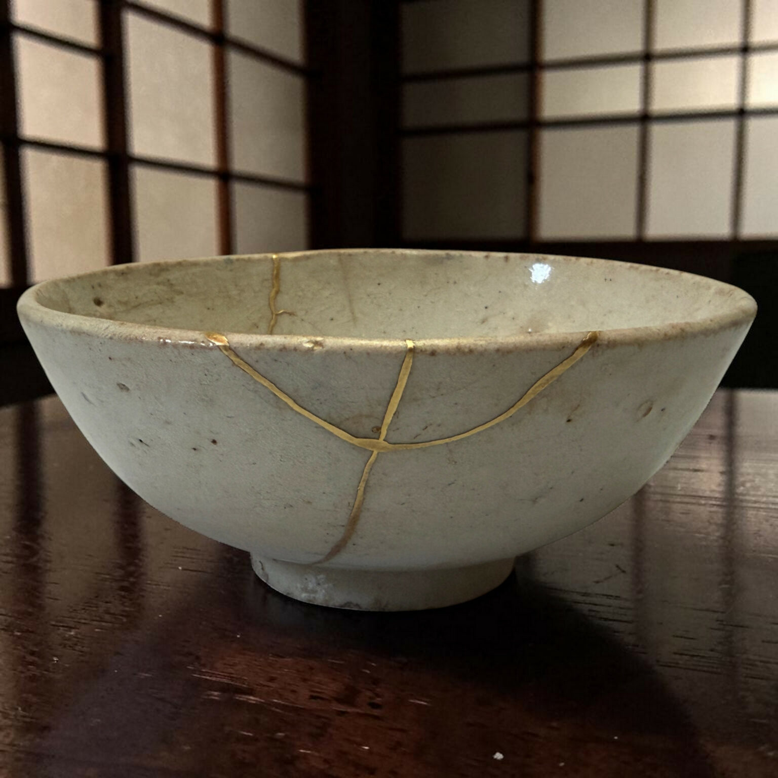 Ceramic bowl with a braided cord looped around its rim on a dark wooden table; a geometric grid backdrop in the background.