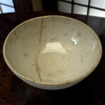Light gray speckled ceramic bowl resting on a dark wooden table, photographed from the top edge view with seam lines visible along the glaze.