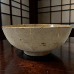 A light, crackled ceramic bowl with a pale glaze rests on a dark wooden table.