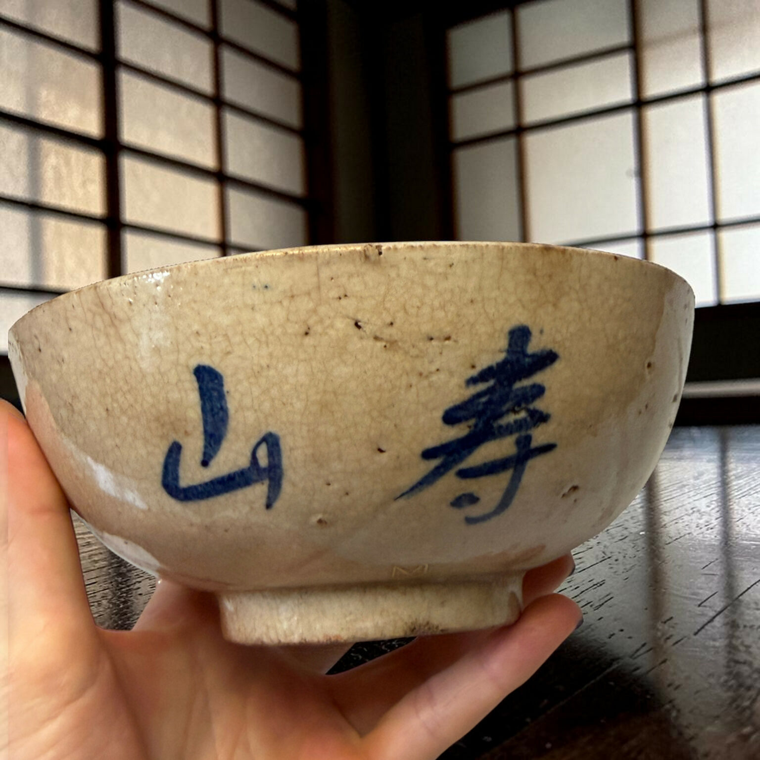 Close-up of a speckled ceramic bowl with blue writing being held by a child's hand, with a tiled wall in the background.