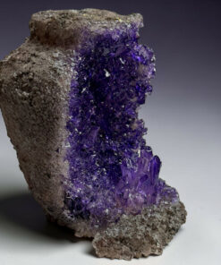 Purple amethyst crystal cluster growing from a rough brown rock surface.