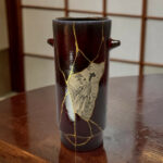 Dark ceramic vase with gold kintsugi cracks on a wooden table surface