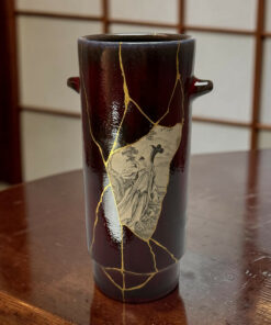 Dark ceramic vase with gold kintsugi cracks on a wooden table surface