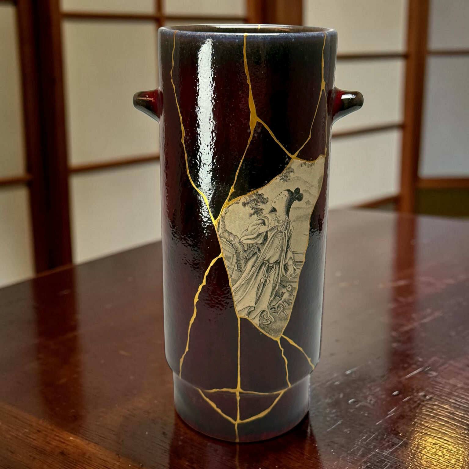 Close-up of a black ceramic vase with gold crackle seams and a painted design, sitting on a wooden table.