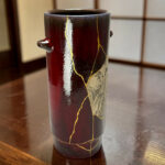 Close-up of a dark maroon ceramic mug with gold crackle glaze patterns on a wooden table surface