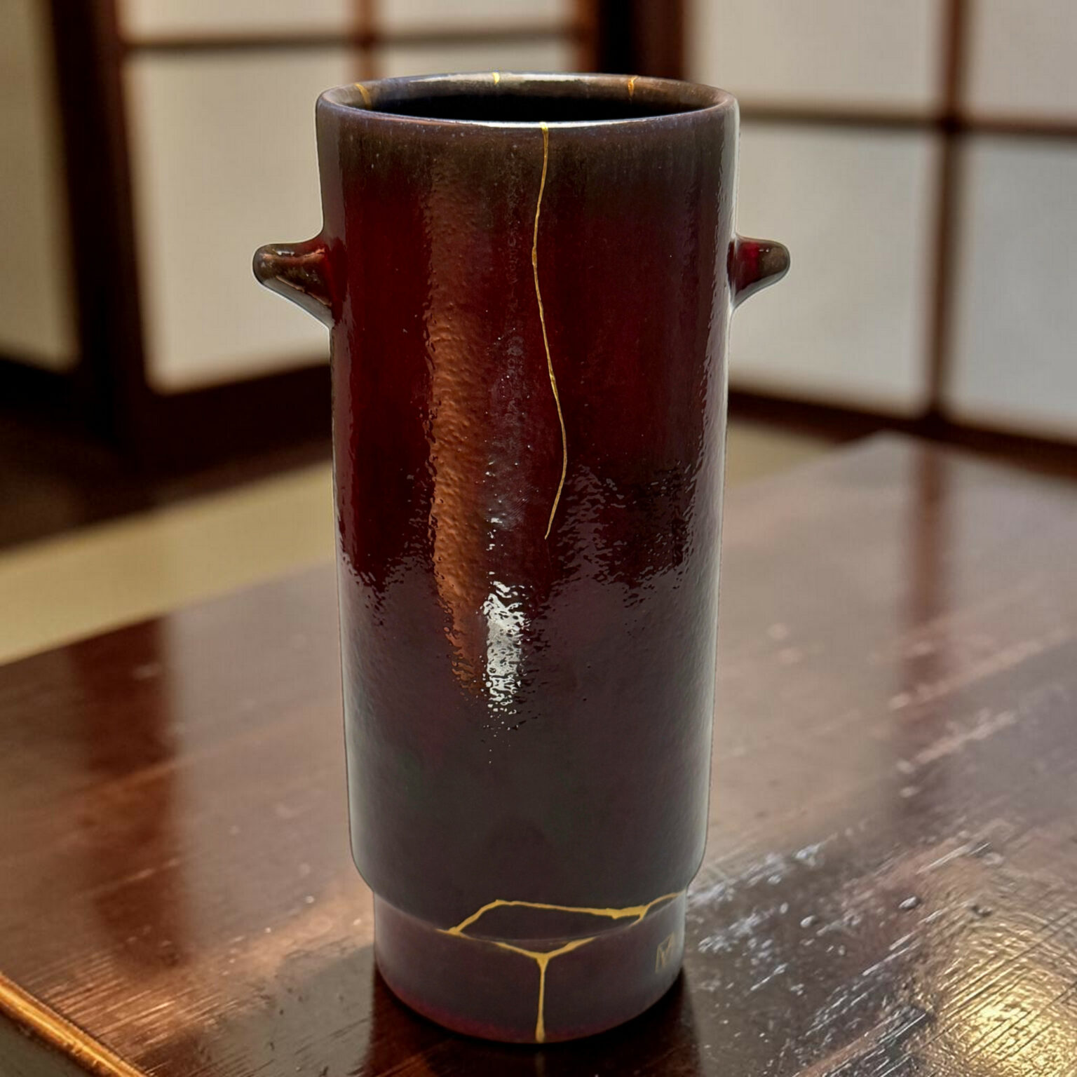 Dark ceramic vase with gold repair seams (kintsugi) on a wooden table, close-up view.