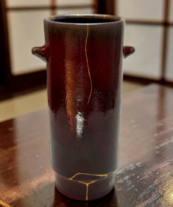 Dark ceramic vase with gold repair seams (kintsugi) on a wooden table, close-up view.