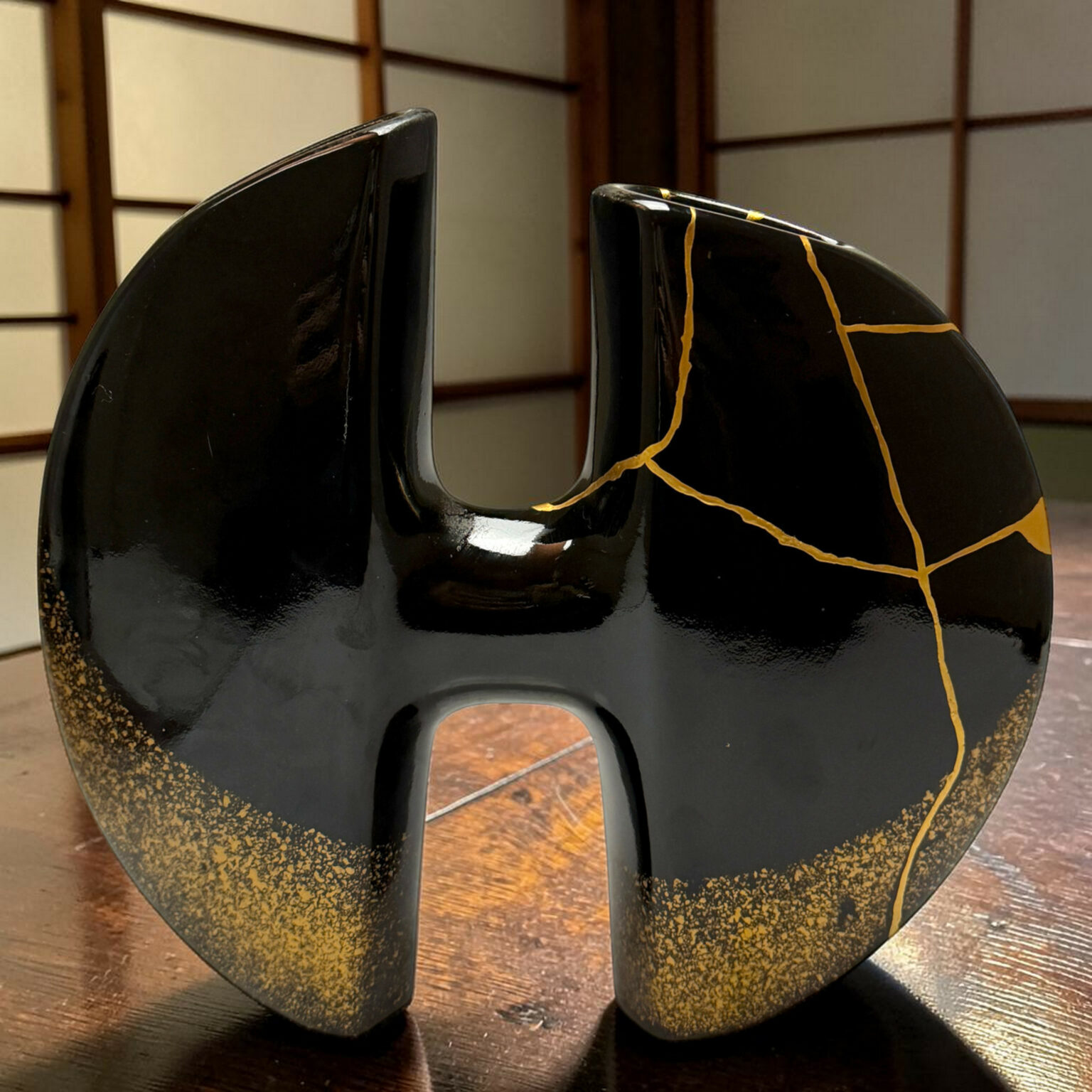 Close-up of two glossy black ceramic vessels with gold vein cracks on a wooden table.