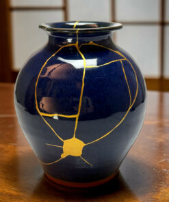 Blue ceramic vase with gold kintsugi cracks on a wooden table surface.