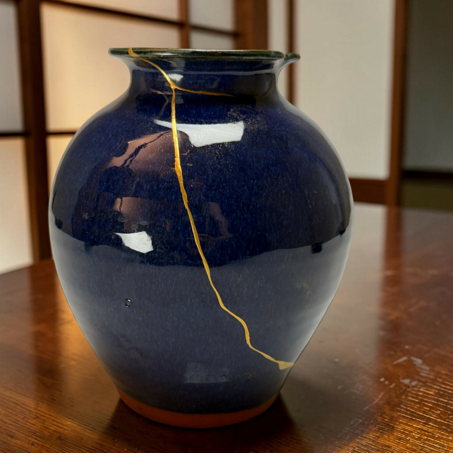 Close-up of a navy blue ceramic vase with a thin gold crack running down its side.