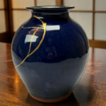 Close-up of a deep blue ceramic vase with gold kintsugi cracks on a wooden table surface.