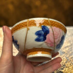 Close-up of a hand holding a small ceramic bowl with blue floral design and gold lines in the glaze.