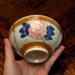 Close-up of a porcelain decorative egg with blue flowers and gold geometric detailing being held by hands.