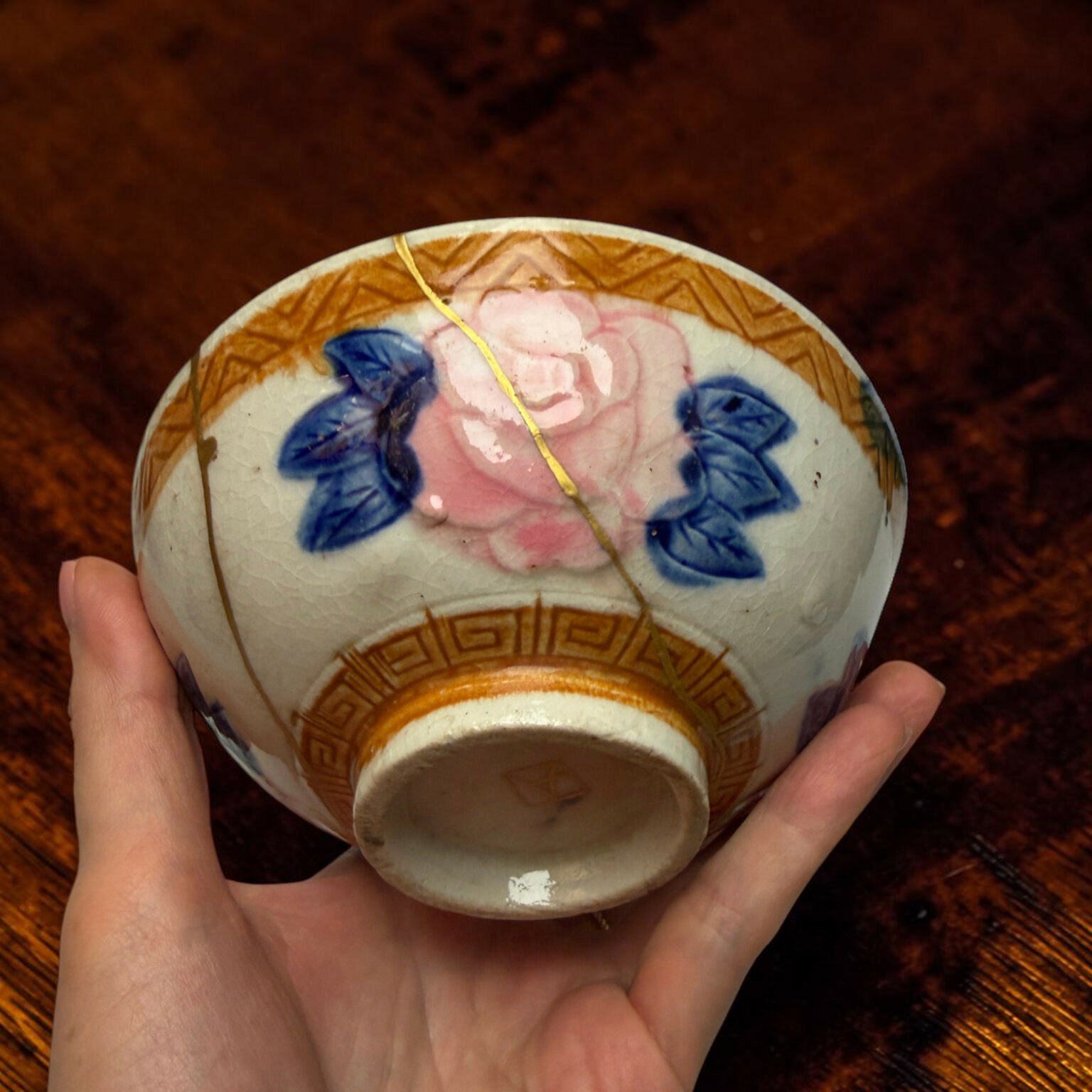 Close-up of a porcelain decorative egg with blue flowers and gold geometric detailing being held by hands.