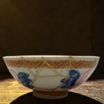 Ceramic hanging bowl with blue floral patterns and yellow cords, resting on a wooden surface.
