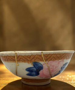 Decorative ceramic hanging bowl with blue and pink floral pattern, suspended by strings against a warm blurred background.