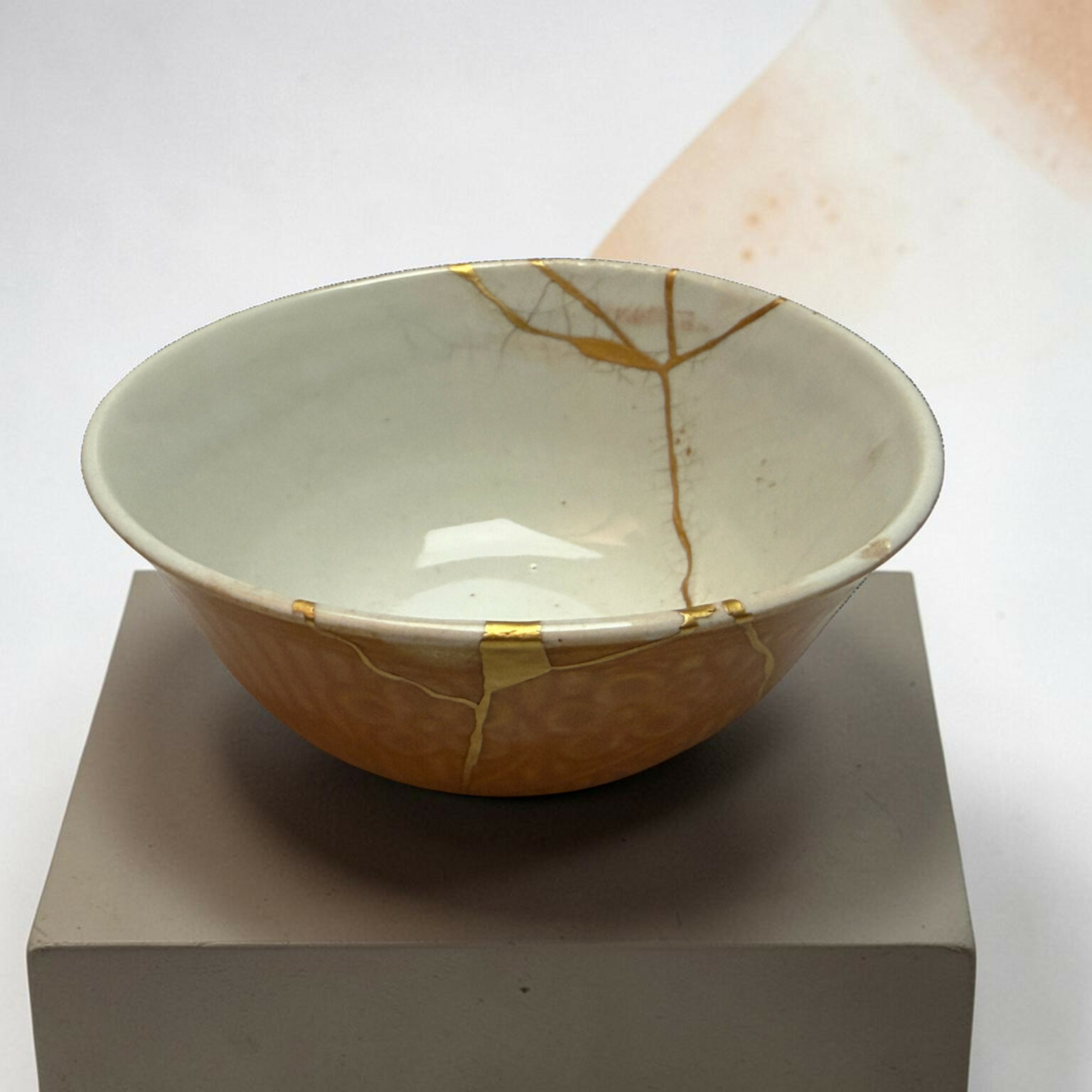 Ceramic bowl repaired with gold kintsugi on a gray display plinth against a light background.