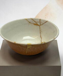 Ceramic bowl repaired with gold kintsugi on a gray display plinth against a light background.