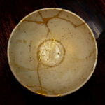 Ceramic plate with gold-filled cracks (kintsugi) on a dark wooden table, close-up view
