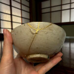 Close-up of hands holding a smooth, gray round stone with gold painted seams.