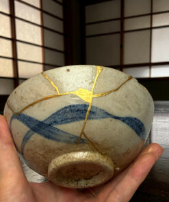 Hands cradle a smooth stone with gold-vein patterns against a wooden grid backdrop, close-up view.