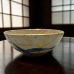 Close-up of a white ceramic bowl with gold decorative lines resting on a dark wooden table, background out of focus.