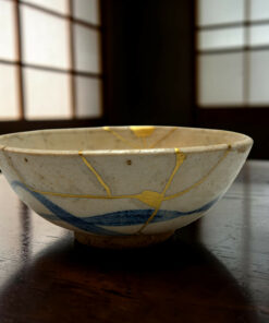 Close-up of a white ceramic bowl with gold decorative lines resting on a dark wooden table, background out of focus.