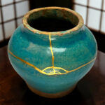 Close-up of a turquoise ceramic vase with gold decorative lines around the rim and a dark interior opening.