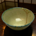 Close-up of a green glazed ceramic bowl with a yellow string wrapped around it on a dark wooden surface.