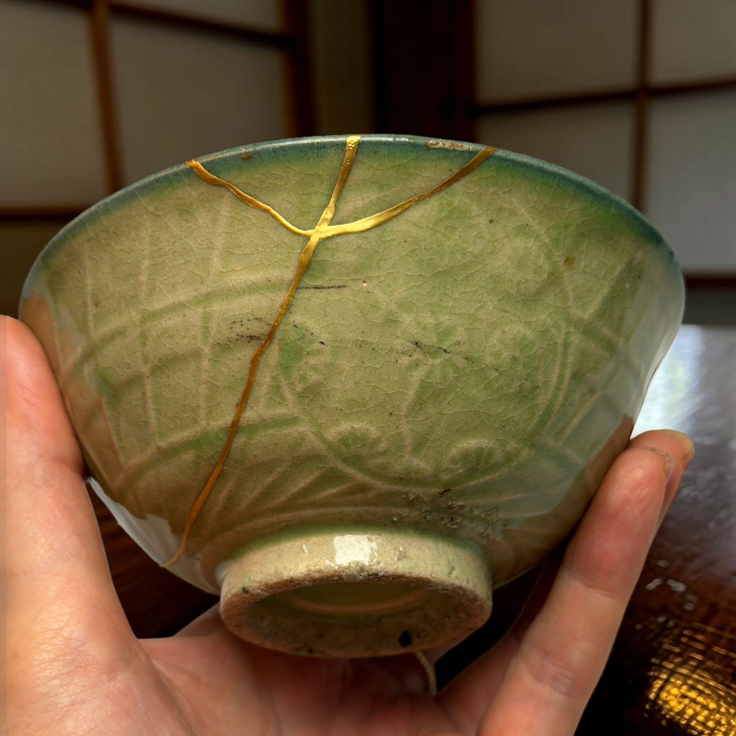 Green ceramic bowl with gold kintsugi cracks, being held by a person in close-up view.