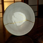 Close-up of a light gray ceramic plate on a dark wooden table with gold string wrapped around it in a decorative pattern