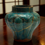 Close-up of a turquoise ceramic vase with crackled glaze and gold lines, resting on a dark wooden table.