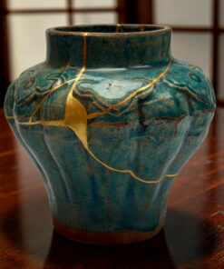 Close-up of a teal ceramic vase with gold crackle lines and carved patterns on a dark wooden table surface.