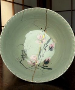 Close-up of a mint-green ceramic plate with a gold crack line and pink floral pattern on a wooden surface.