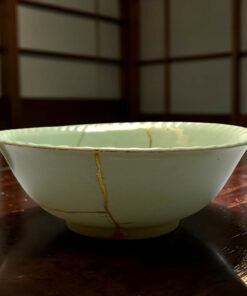 Close-up of a white ceramic bowl with a gold vertical line design, resting on a dark wooden table.