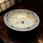 A ceramic bowl with a blue rim and gold crack lines, resting on a dark wooden table.