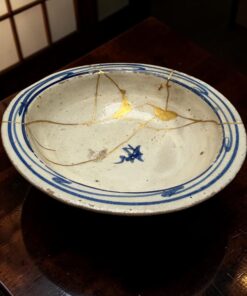 A ceramic bowl with a blue rim and gold crack lines, resting on a dark wooden table.