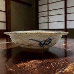 Close-up of a white ceramic bowl with blue decoration on a dark wooden table, flour splatters around it.