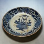 Close-up of a blue-and-white porcelain plate with intricate floral patterns and a thin gold rim, tied with a delicate gold string.