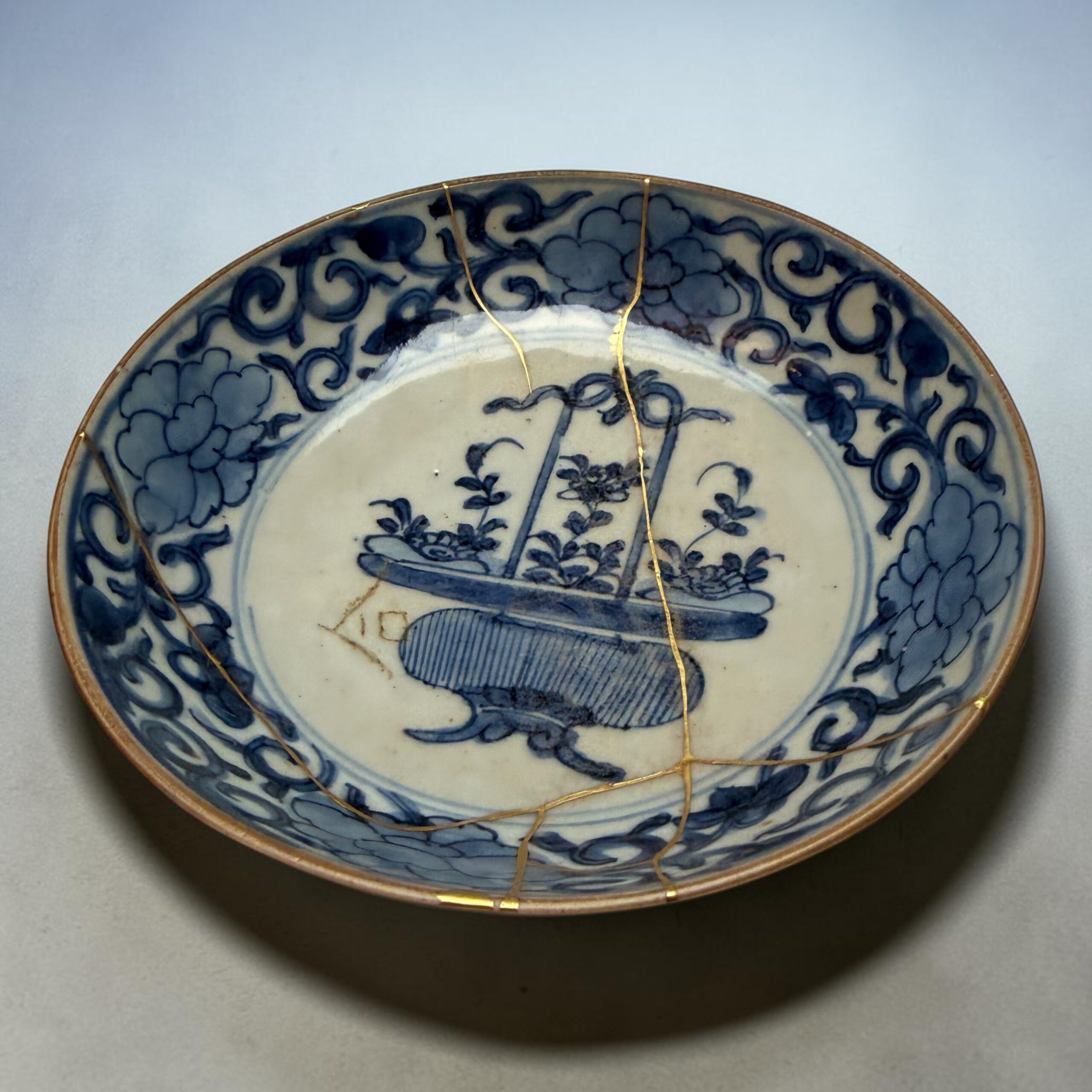 Close-up of a blue-and-white porcelain plate with intricate floral patterns and a thin gold rim, tied with a delicate gold string.
