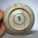 Close-up of a porcelain plate with gold-filled cracks (kintsugi) being held by a hand.